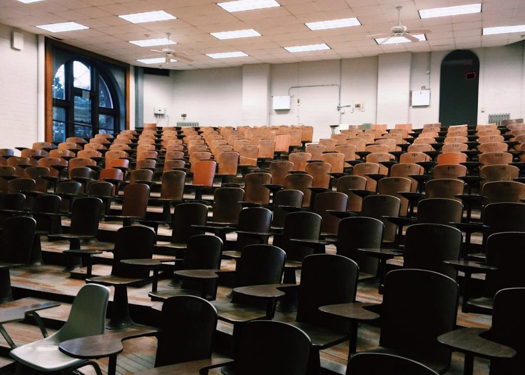 room-chair-lot-356065 Empty university lecture hall with wooden chairs and large windows.